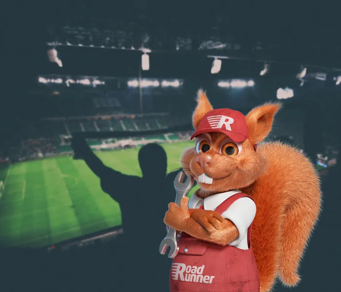 A cartoon squirrel in overalls and a hat, holding a wrench, stands in a football stadium with a cheering fan in the background.