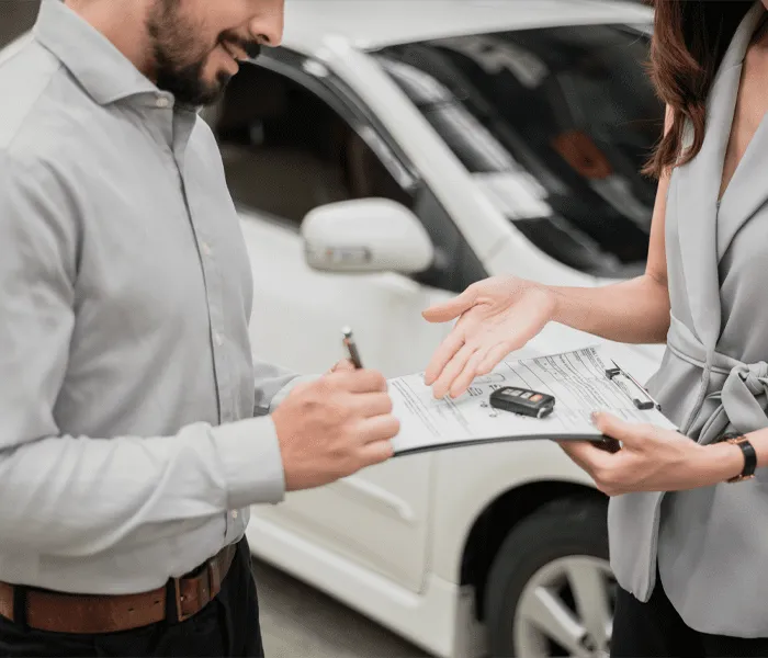 Two people standing next to a car, signing a document on a clipboard while exchanging car keys.