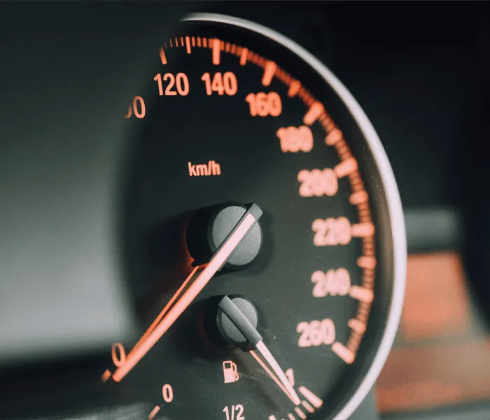 Close-up of a car's analog speedometer showing a speed of about 120 km/h, with a fuel gauge indicator visible below.