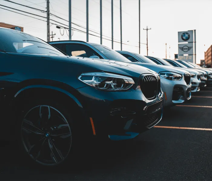 A row of black and silver cars is parked in a dealership lot, with a BMW sign visible in the background.