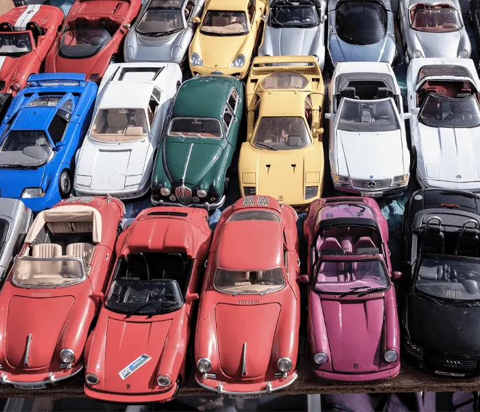 A collection of various colorful toy cars, including red, yellow, blue, and green models, displayed in tightly packed rows.