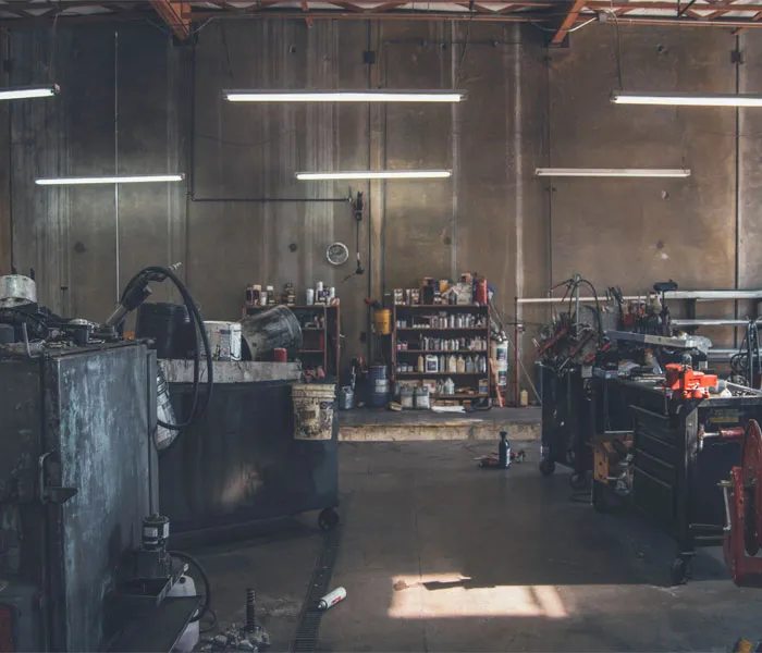 A dimly lit mechanic's garage with workstations, tools, equipment, and shelves filled with various supplies and parts.