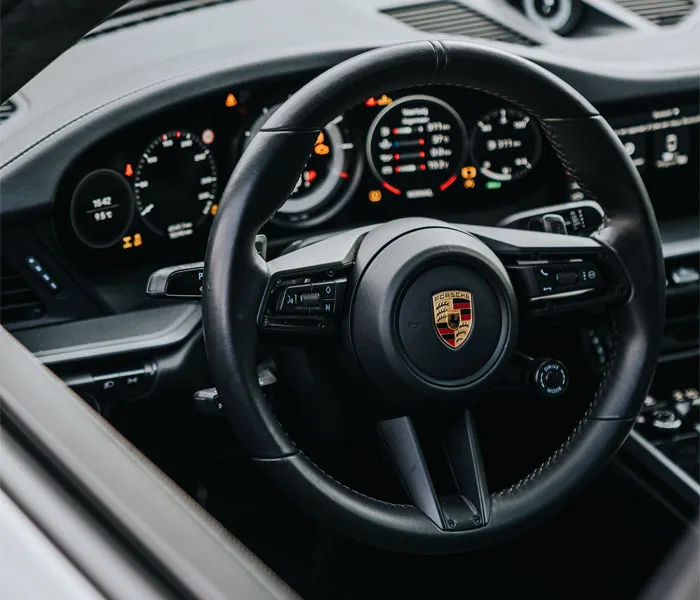 Close-up of an interior car dashboard and steering wheel with multiple controls and illuminated displays.