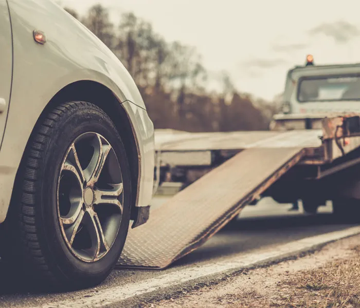 A car being loaded onto a tow truck with a ramp by the roadside.